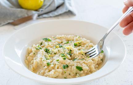 Risotto mit Zitrone und Petersilie wird mit einer Gabel vom Teller genommen.