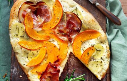 Pizza bianca mit Kürbis und Kartoffeln auf einem Holzbrett.