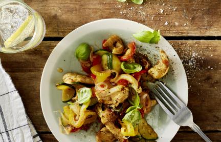 Buntes Gemüse mit Hähnchen und Basilikumblättern auf einem Teller.