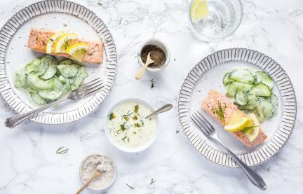 Lachs mit Gurkensalat und Kräuterremoulade auf einem Teller.