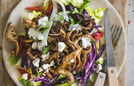 Teller mit Fleisch und Salat auf Holzbrett