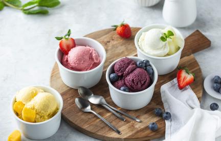 Fruchteis zu Kugeln portioniert in kleinen Schälchen, die auf einem Holzbrett stehen.