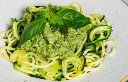 Zoodles mit Avocadopesto angerichtet n einem tiefen Teller, darauf Basilikumblätter