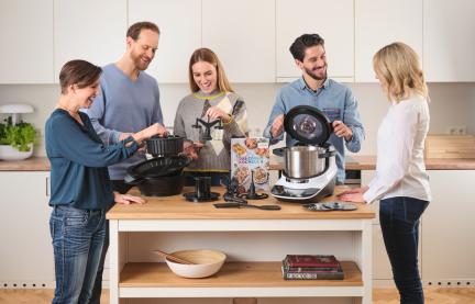 Der Cookit steht mit seinen Tools auf der Küchezeile und fünf Leute betrachten diese. 