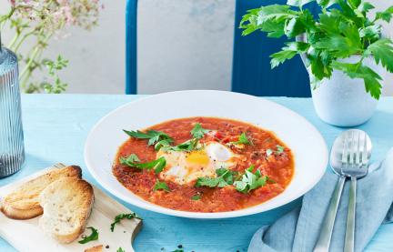 Shakshuka in einem hellen Teller mit Ei und Basilikum.