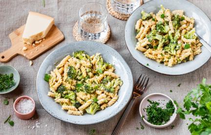 One-Pot-Pasta mit Brokkoli in hellen Schüsseln auf einem gedeckten Tisch.
