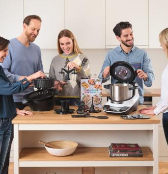 Der Cookit steht mit seinen Tools auf der Küchezeile und fünf Leute betrachten diese. 