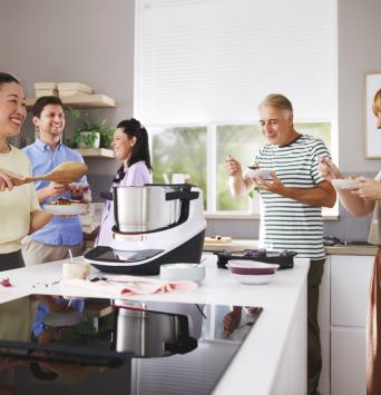 Fünf Personen stehen um den Cookit herum und probieren die zubereitete Speise. 