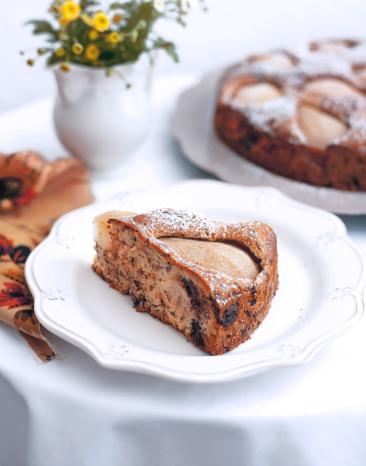 Ein Birnen-Walnusskuchen vor einem weißen Hintergrund, mit Puderzucker bestreut