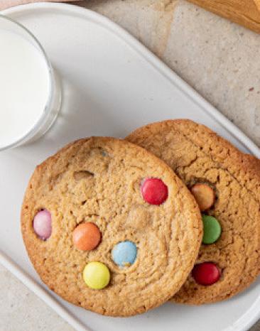 Cookies mit bunten Schokolinsen auf zwei Teller mit einem Glas Milch. Cookies mit bunten Schokolinsen auf zwei Teller mit einem Glas Milch.