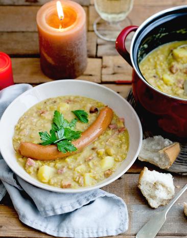 Deftige Erbsensuppe mit Wiener Würstchen in einem Teller, daneben der Suppentopf.