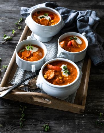 Deftiges Wurstgulasch in vier Suppenschalen auf einem Tablett.