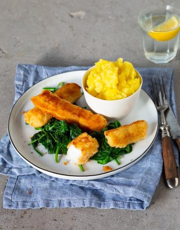 Fischstäbchen, Spinat und Kartoffelpüree auf Teller mit Wasserglas und Besteck