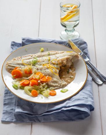 Teller mit Scholle und Gemüse, blaues Tuch, Besteck und Wasserglas