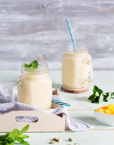 Gelber Mango-Lassi mit Kokosmilch in zwei Gläsern mit Strohhalm.