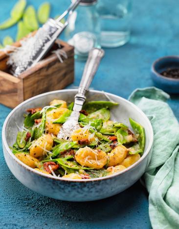 Gnocchi mit Zuckerschoten und getrockneten Tomaten in Parmesansauce in einer Schale 