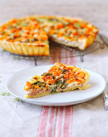 Ein Quichestück auf einem Teller vor der angeschnitten Quiche. 