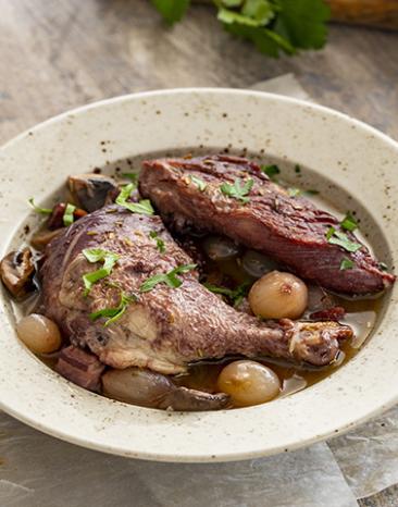 Hahn in Rotweinsoße (Coq au vin) auf einem Teller angerichtet.