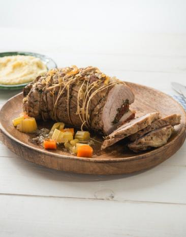 Kalbsrollbraten mit Kräuterfüllung und Gemüse auf einem Teller.