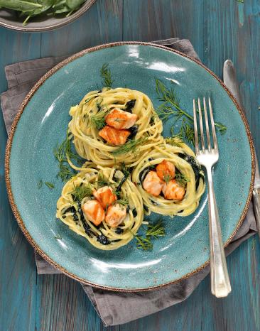 Lachs-Spaghettinester mit Gorgonzola und Spinat auf einem Teller.