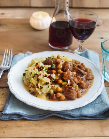 Lamgulasch mit Stampf auf einem Teller angerichtet zu einem Glas Rotwein. 