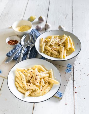 Zwei Teller Nudeln mit Käsesauce auf weißem Holztisch.