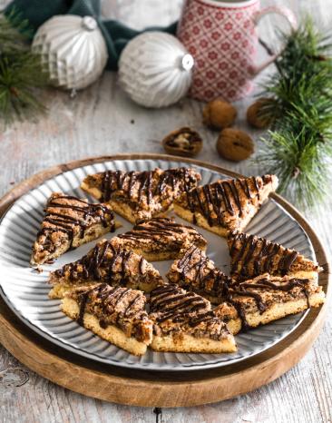 Nussecken vor winterlichem Hintergrund auf einem Teller verteilt und mit Schokolade verziert.