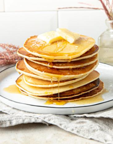 Pancakes amerikanisch übereinander gestapelt mit Butter und Sirup auf einem Teller.