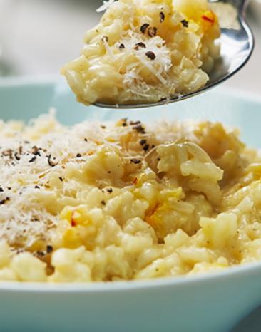 Risotto Milanese wir mit einem Löffel aus einer Schale genommen. Risotto Milanese wir mit einem Löffel aus einer Schale genommen.