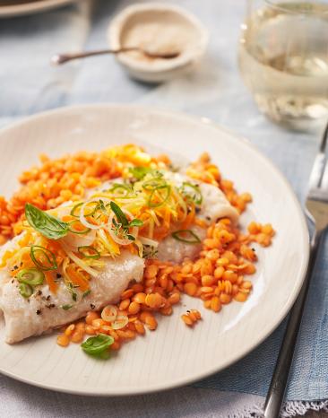 Rotbarschfilet mit Gemüsehaube und roten Linsen auf einem Teller angerichtet.