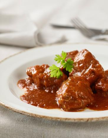 Saftgulasch nach Wiener Art auf weißem Teller mit Petersilie garniert. Saftgulasch nach Wiener Art auf weißem Teller mit Petersilie garniert.
