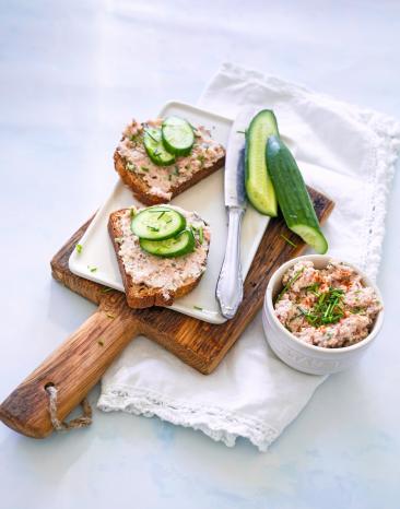 Zwei Scheiben Brot mit Streichwurst und Gurke auf Holzbrett.