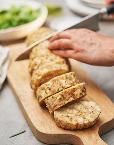 Serviettenknödel wird auf einem Holzbrett in Scheiben geschnitten. Serviettenknödel wird auf einem Holzbrett in Scheiben geschnitten.
