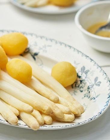 Stangenspargel mit neuen Kartoffeln und Zitronenpfeffer-Butter auf einem Teller. Stangenspargel mit neuen Kartoffeln und Zitronenpfeffer-Butter auf einem Teller.