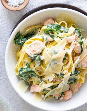 Tagliatelle mit Lachs in Spinat-Sahnesauce auf zwei Tellern angerichtet.