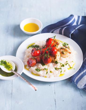 Zitronenrisotto mit Jacobsmuscheln und Kirschtomaten auf einem Teller.