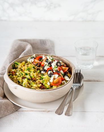 Zucchini-Bulgur mit Feta und Tomaten in Schüssel mit Besteck Zucchini-Bulgur mit Feta und Tomaten in Schüssel mit Besteck