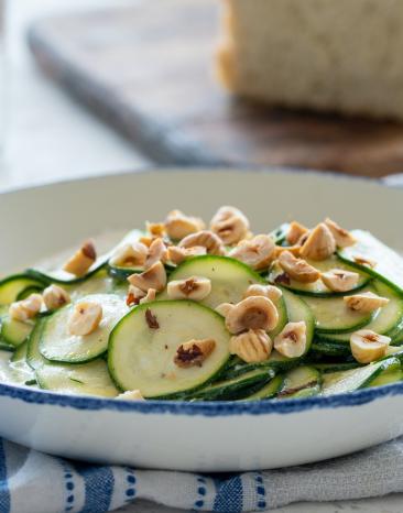 Marinierte Zucchini mit gerösteten Haselnüssen und Ricotta in einem tiefen Teller angerichtet.