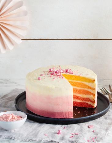 Rosa Ombré-Cake Zitrone-Joghurt-Creme angeschnitten auf einem Servierteller.