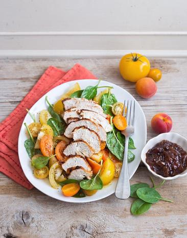 Gelber Sommersalat mit gegrillter Hähnchenbrust Sous-vide und Schalottenchutney auf einem Teller angerichtet.