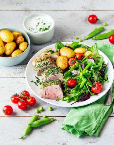 Kräuter-Schweinefilet mit Ofenkartoffeln und Bohnensalat auf einem Teller.