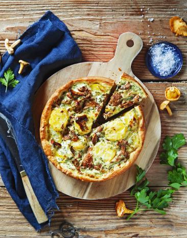 Quiche mit Kartoffeln und Pfifferlingen auf einem Holzbrett.