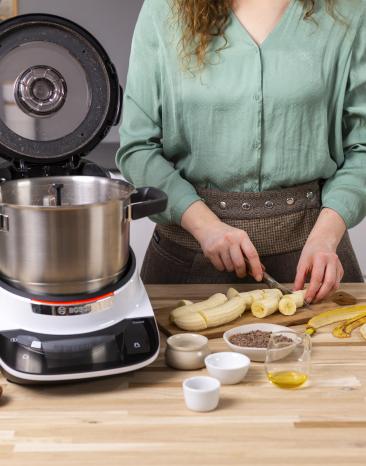 Bananenbrot-Zutaten neben de Cookit: Bananen werden vorbereitet Bananenbrot-Zutaten neben de Cookit: Bananen werden vorbereitet