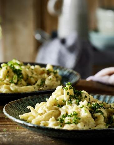 Käsespätzle angerichtet auf einem rustikal gedeckten Tisch Käsespätzle angerichtet auf einem rustikal gedeckten Tisch