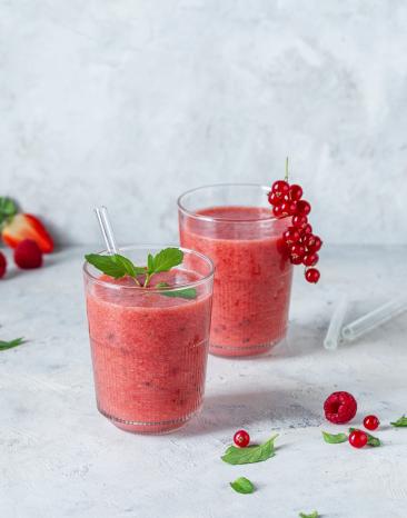 Roter Smoothie in zwei Gläsern mit Beeren garniert.