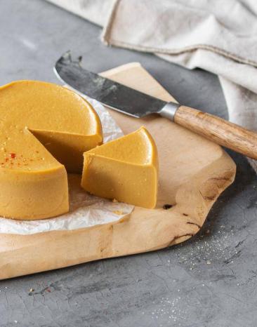 Veganes Käsetötchen angeschnitten auf einem Holzbrett Veganes Käsetötchen angeschnitten auf einem Holzbrett