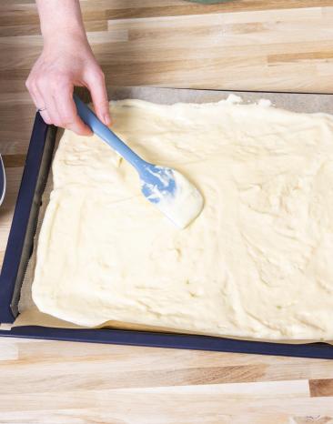 Biskuitteig wird auf einem Backblech mit Backpapier verteilt. Biskuitteig wird auf einem Backblech mit Backpapier verteilt.