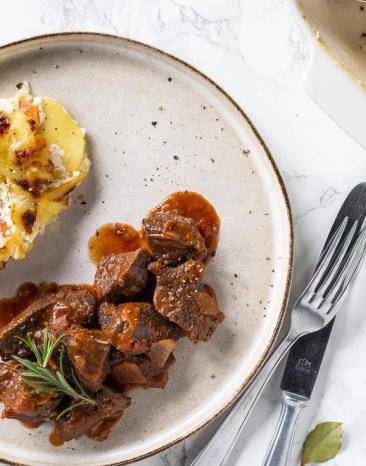 Portion von Lammschmortopf und daneben Kartoffel-Karotten-Gratin auf einem weißen Teller Portion von Lammschmortopf und daneben Kartoffel-Karotten-Gratin auf einem weißen Teller