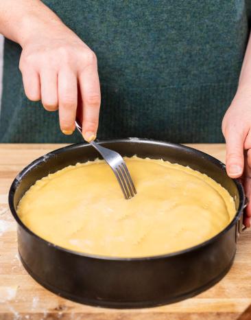 Gedeckter Apfelkuchen - Teig wird mit einer Gabel eingestochen.