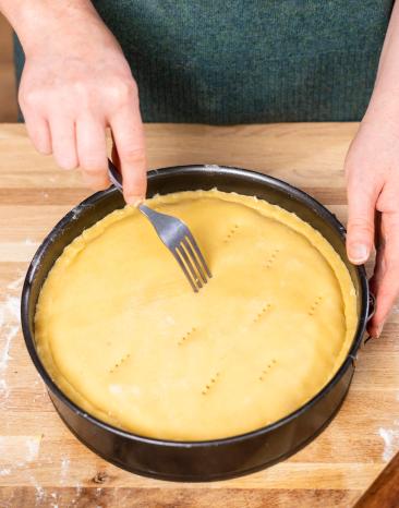 Teig vom gedeckten Apfelkuchen wird vor dem Backen mit einer Gabel eingestochen. Teig vom gedeckten Apfelkuchen wird vor dem Backen mit einer Gabel eingestochen.